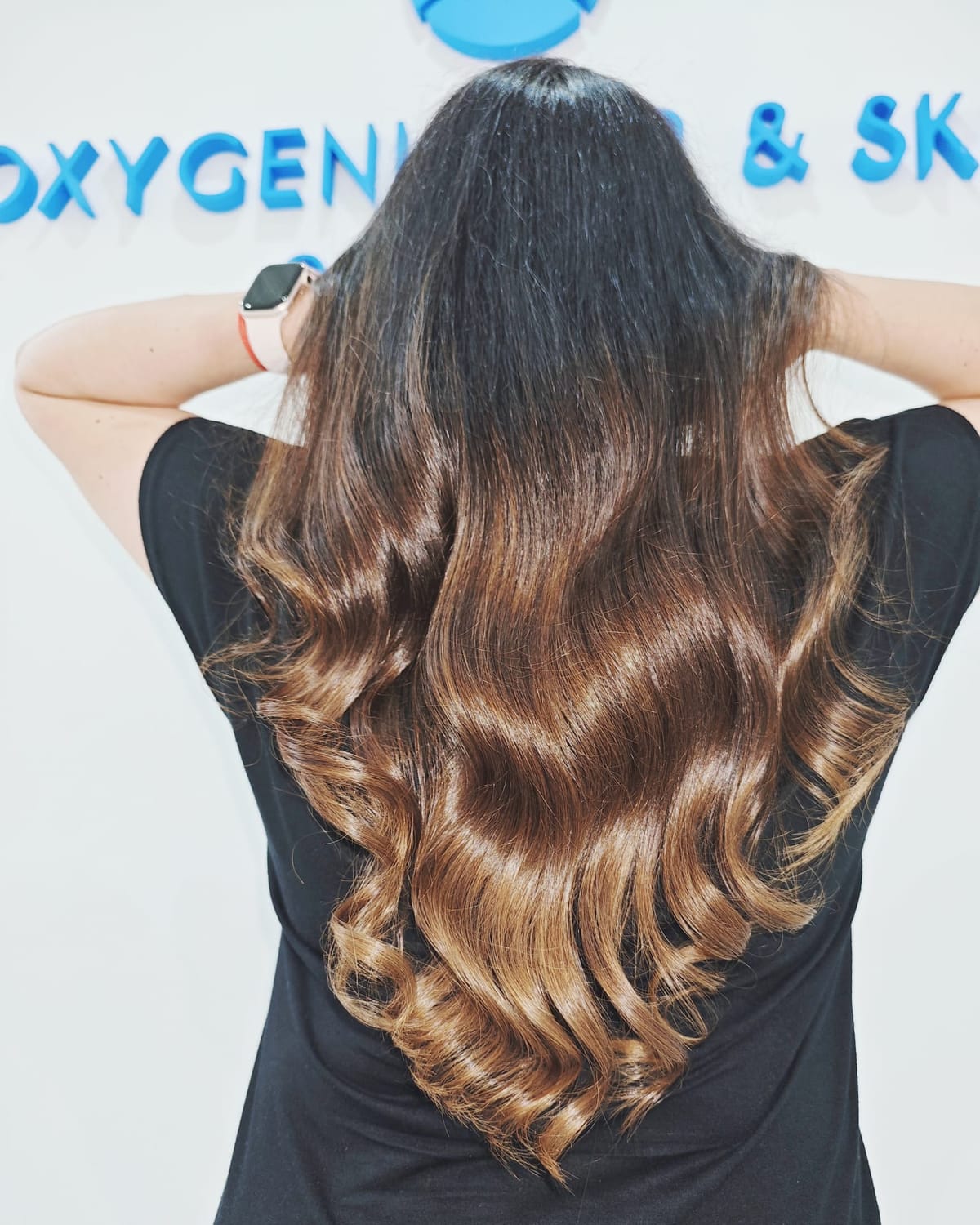 Rückansicht dunkelbraunen Haars mit Karamell-Längen und definierten glänzenden Locken, gestylt im Oxygeni Hair Salon Wien